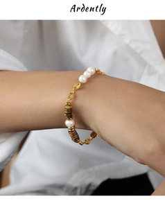 Detail of tiger eye and pearl necklace on wrist featuring gold chain and toggle clasp