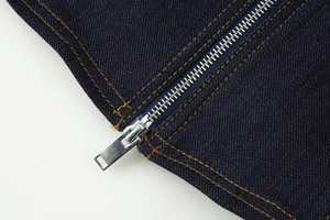 Détail d'une fermeture éclair argentée sur veste en jean bleu foncé avec surpiqûres orange