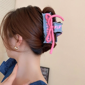 Detail of blue denim bow hair claw with pink woven rope and artistic lettering