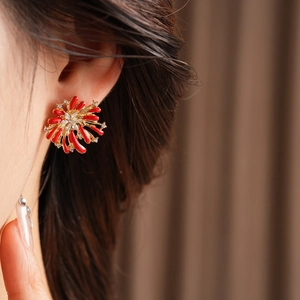 Close-up of red firework earrings with gold plating and diamonds worn on an ear