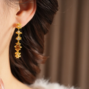 Detailed close-up of tiger eye stone earrings with pearls and zircons on ear