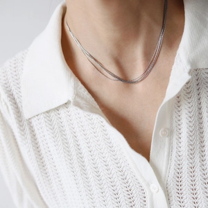 Close-up of layered silver snake chains on model wearing a white knit shirt