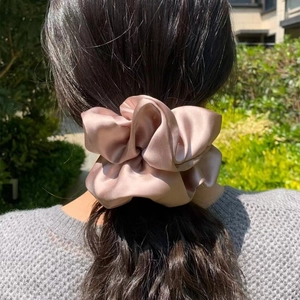 Elegant champagne satin scrunchie shown in a low bun hairstyle under natural sunlight
