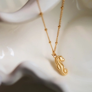 Close-up of golden seahorse pendant with satellite chain on white ceramic base