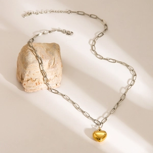 Close-up of golden heart pendant on silver paperclip chain against a textured stone