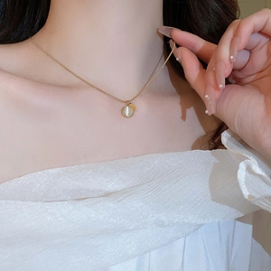 Close-up of a gold snake chain necklace with a round cat eye stone and metal charm