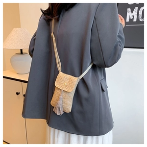 Straw woven crossbody phone bag with fringe detail worn by a model in a minimalist setting