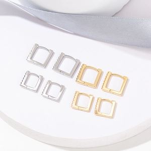 Minimalist square zircon earrings in gold and silver finishes on a white stone base