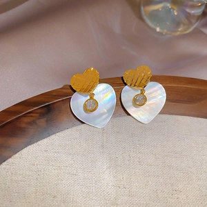 Dettaglio macro di orecchini a cuore placcati oro 24k con zircone e madreperla cangiante