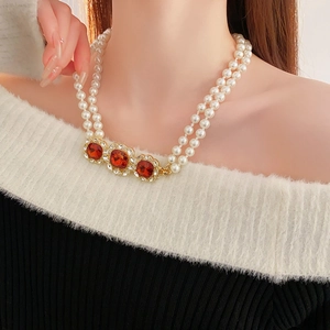 Detail of double-layer pearl necklace with three amber red gemstone pendants on black knit