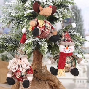 Close-up of plush Santa and elk ornaments with plaid fabric on a snowy Xmas tree