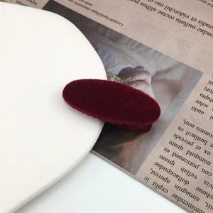 Macro detail of a refined burgundy velvet oval hair clip on a minimalist white plate