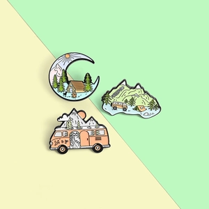 Detail of three enamel outdoor camping pins featuring mountains, cabins, and travel vans