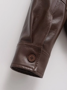 Detail of dark brown leather jacket cuff showing fine stitching and button texture