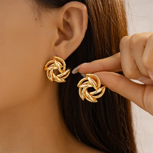 Close-up of golden geometric spiral earrings held by hand and worn by a model