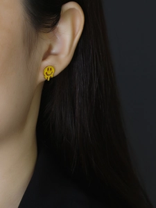 Close-up of a trendy S925 silver stud earring with yellow melting smiley face design
