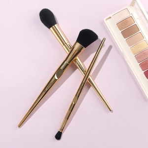 Macro detail of three gold makeup brushes with black bristles and metal handles