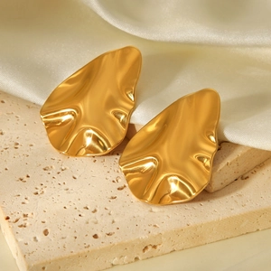 Detail of 18k gold irregular hammered metal earrings on a beige stone and silk background