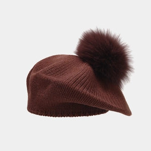 Detail of dark brown knitted beret featuring a fluffy pompom and vertical stitch texture