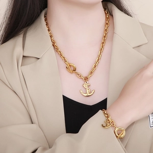 Detail of gold nautical anchor pendant necklace and bracelet set worn on beige blazer