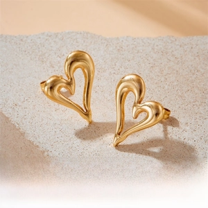 Detailed macro view of gold-plated hollow heart earrings on a beige stone surface