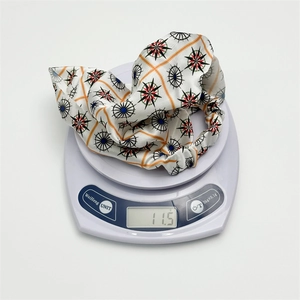Elastic white satin headscarf featuring orange grid and compass prints shown on a scale