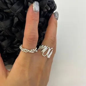 Detail of silver irregular wrap and double-layered beaded rings against a black bag