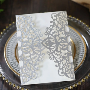 Macro shot of silver glitter laser-cut floral wedding invitation on a glass plate