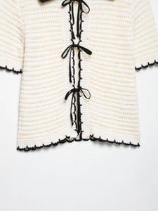 Close-up of white crochet knit top featuring black ribbon ties and wavy contrast trim
