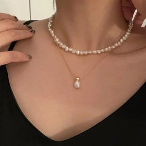 Close-up of double-layer necklace with white pearls and gold chain on a model's neck