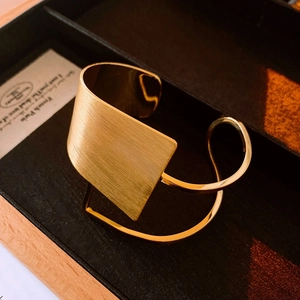 Detail of gold-plated cuff bracelet featuring horizontal brushed texture and sleek open design