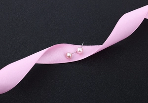 Macro shot of small pink freshwater pearl earrings on black background with pink silk ribbon