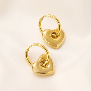 Close-up of polished gold heart earrings on elegant beige silk fabric texture