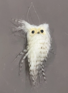 Detail of a white faux fur owl ornament with striped wings and a clear hanging string