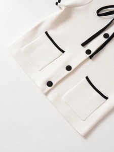 Detail of white knit top featuring black contrast trim pockets and elegant buttons