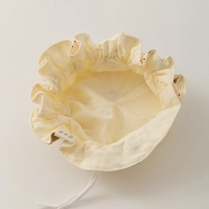 Detail of soft cream cotton drawstring baby hat bag with delicate fabric folds and tag