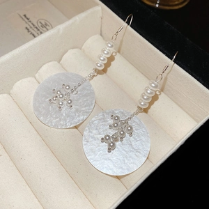 Detail of drop earrings with white pearls and a large round shell pendant on velvet surface