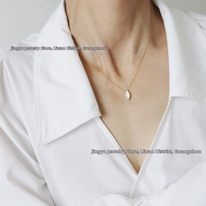 Close-up of 18K gold-plated oval shell pendant necklace on white shirt collar