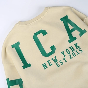 Détail du col rond côtelé et de l'imprimé vert ICA NEW YORK sur le sweat beige