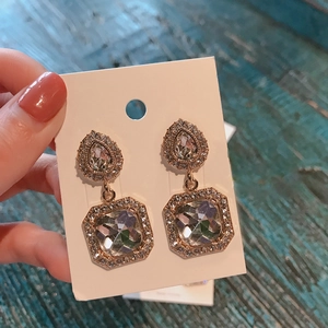 Close-up of geometric gold-plated earrings with clear crystals held against a green wood background