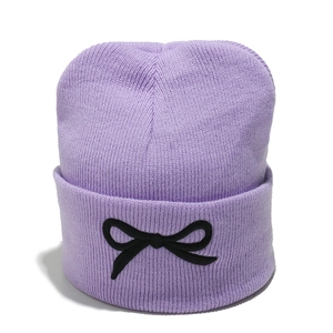 Détail du bonnet en tricot lavande avec un nœud noir décoratif sur le bord plié
