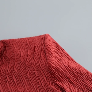 Detail of red pleated fabric texture on a long sleeve top with intricate crinkle patterns