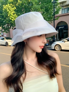 Detail of white pleated sun hat with a large bow decoration in an outdoor setting