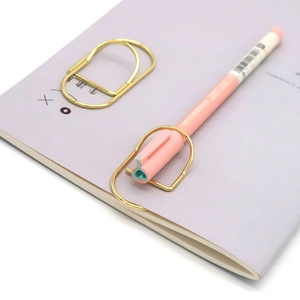Large gold metal paperclip bookmark on a lavender notebook with a pink pen accessory