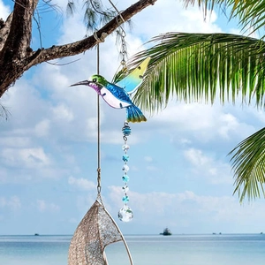 Vibrant hummingbird suncatcher with crystal ball hanging on a palm tree by the sea