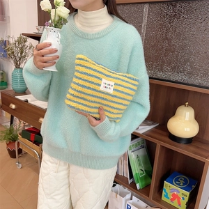 Detail of plush yellow and blue striped makeup bag with soft texture and brand label