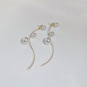 Detail of long gold earrings featuring cascading white pearls on curved metal fringe