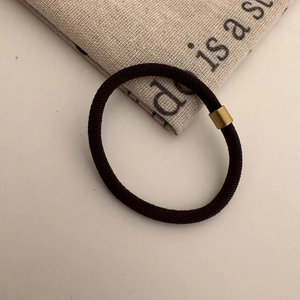 Detail of high-elasticity brown hair tie with a decorative metallic gold connector tube