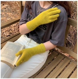 Close-up of yellow knitted gloves worn by a model holding a book in an autumn setting