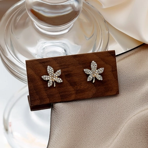 Detailed close-up of golden maple leaf stud earrings inlaid with white crystals